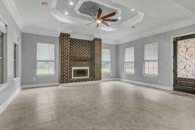 unfurnished living room featuring crown molding, a brick fireplace, ceiling fan, a wealth of natural light, and a tray ceiling