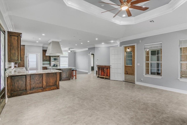 kitchen featuring stainless steel microwave, a raised ceiling, crown molding, light stone counters, and extractor fan