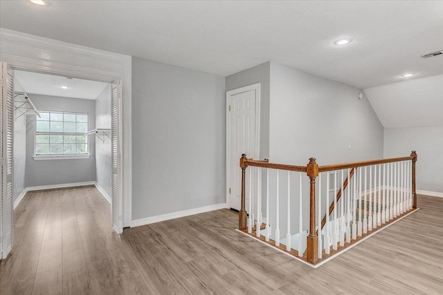 hall featuring a textured ceiling, light hardwood / wood-style floors, and vaulted ceiling