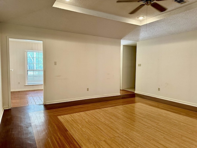 empty room featuring a tray ceiling, ceiling fan, a textured ceiling, and hardwood / wood-style flooring