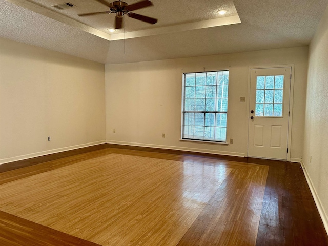 interior space with a textured ceiling, ceiling fan, a raised ceiling, and dark wood-type flooring