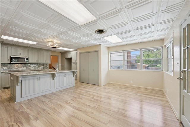 2701 Mcbride Dr, Port Neches, TX 77651 - kitchen featuring stainless steel microwave, gray cabinets, tasteful backsplash, an ornate ceiling, and light wood-style floors