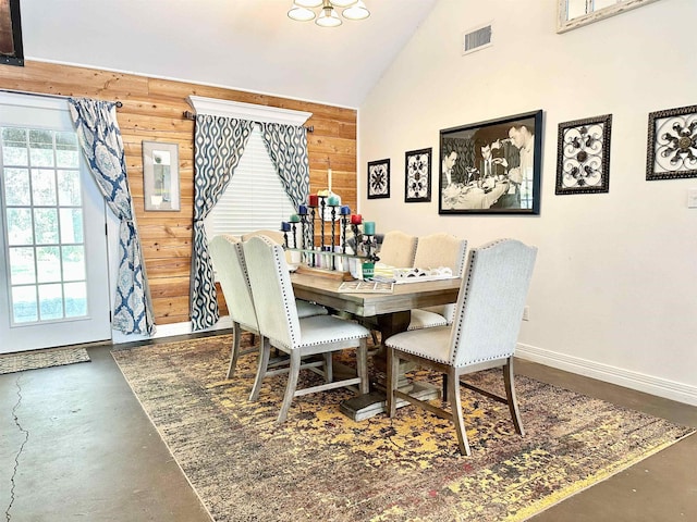dining area with high vaulted ceiling, visible vents, wooden walls, finished concrete flooring, and baseboards