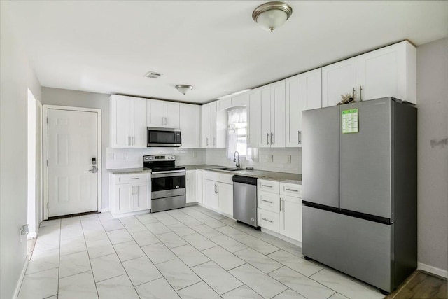 kitchen featuring white cabinetry, sink, stainless steel appliances, light stone counters, and decorative backsplash