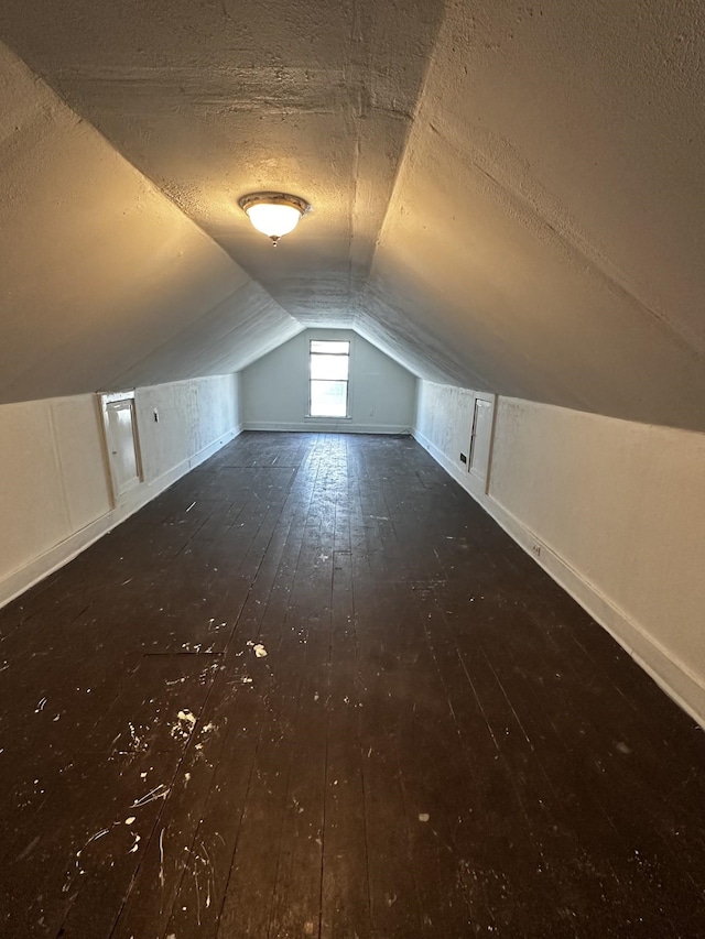 additional living space with a textured ceiling, vaulted ceiling, wood-type flooring, and baseboards