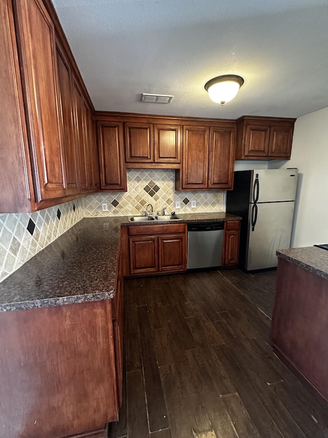 kitchen featuring stainless steel appliances, a sink, visible vents, decorative backsplash, and dark wood-style floors