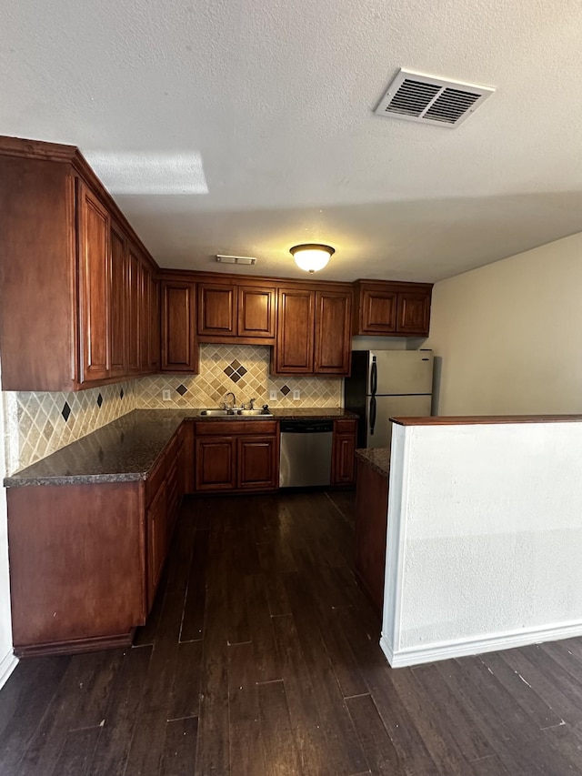 kitchen featuring dark countertops, visible vents, decorative backsplash, appliances with stainless steel finishes, and dark wood-type flooring