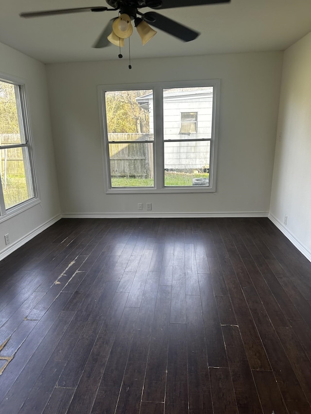 empty room with dark wood-style flooring, a ceiling fan, and baseboards