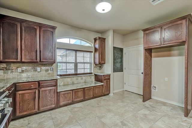 kitchen featuring light stone counters, backsplash, and stainless steel range oven