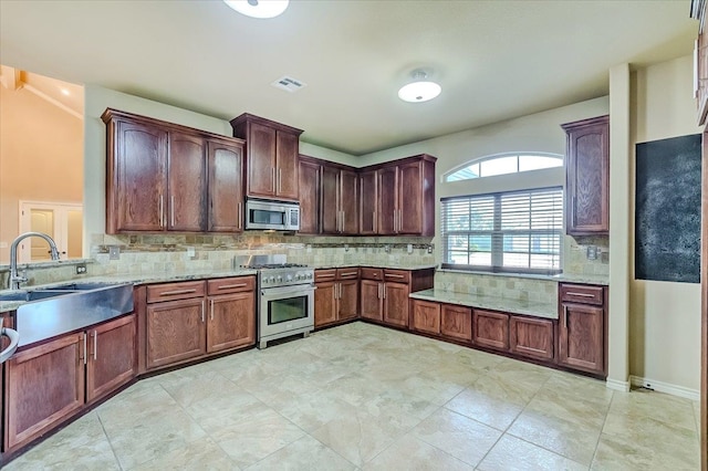 kitchen with backsplash, light stone countertops, sink, and appliances with stainless steel finishes