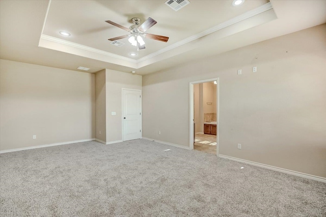 unfurnished bedroom with a tray ceiling, ceiling fan, ensuite bathroom, and light carpet