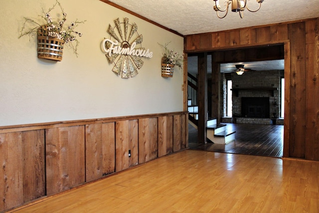 interior space with ceiling fan with notable chandelier, light wood-type flooring, a textured ceiling, and a brick fireplace