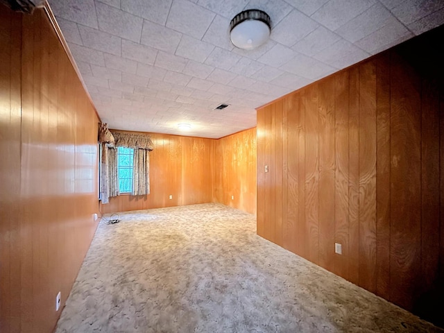 carpeted empty room featuring wood walls