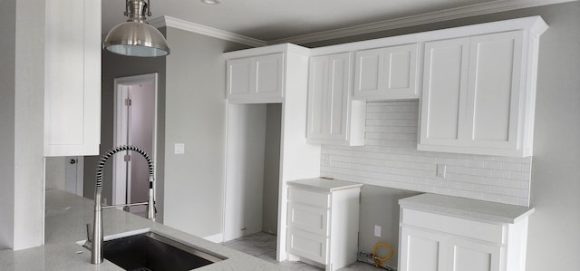 kitchen with backsplash, white cabinetry, ornamental molding, and sink