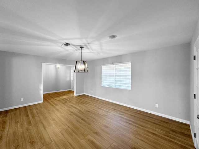 unfurnished room featuring baseboards, a chandelier, and wood finished floors