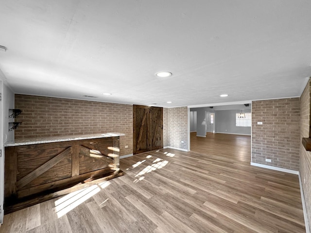 below grade area featuring brick wall, wood finished floors, baseboards, recessed lighting, and a bar