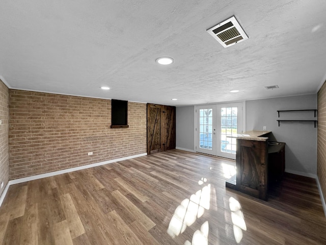 basement with brick wall, baseboards, french doors, wood finished floors, and a textured ceiling