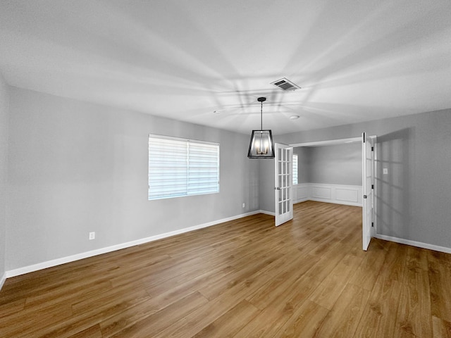 unfurnished dining area featuring wood finished floors, a chandelier, a wainscoted wall, and baseboards