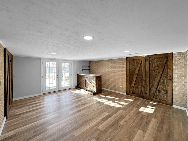unfurnished living room featuring brick wall, a textured ceiling, wood finished floors, baseboards, and french doors