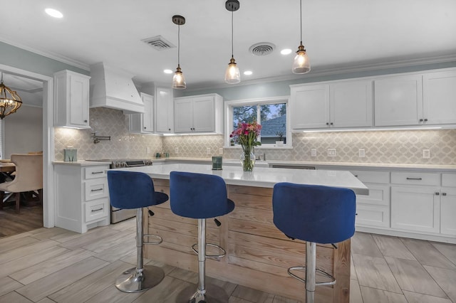 kitchen with custom exhaust hood, a kitchen island, pendant lighting, and white cabinets