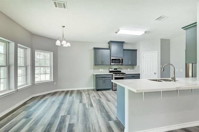 kitchen featuring appliances with stainless steel finishes, decorative light fixtures, sink, gray cabinetry, and a kitchen bar