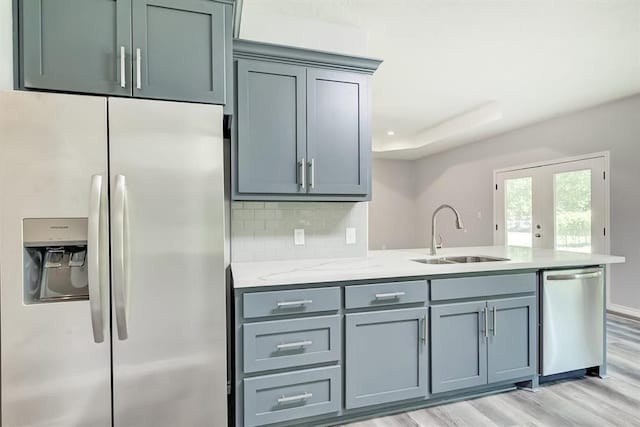 kitchen featuring sink, light stone counters, appliances with stainless steel finishes, light hardwood / wood-style floors, and backsplash