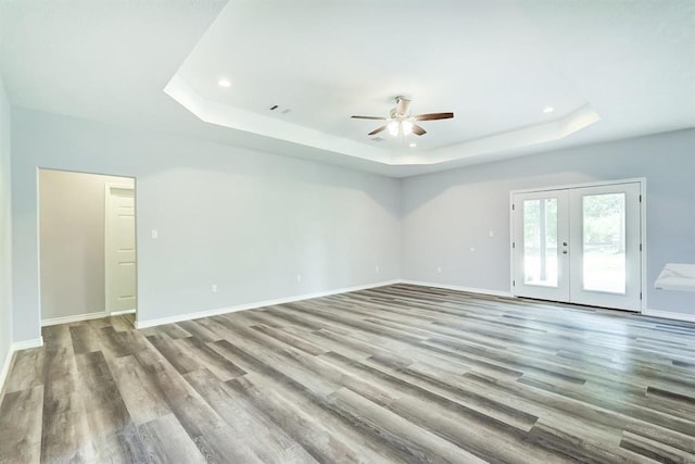 empty room featuring french doors, ceiling fan, a tray ceiling, and light hardwood / wood-style flooring