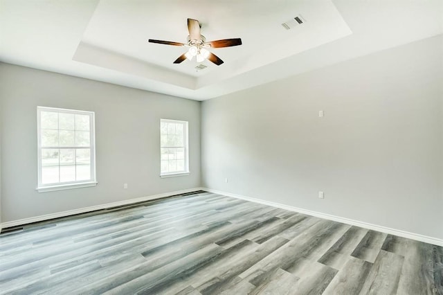 empty room with light hardwood / wood-style flooring, ceiling fan, and a tray ceiling