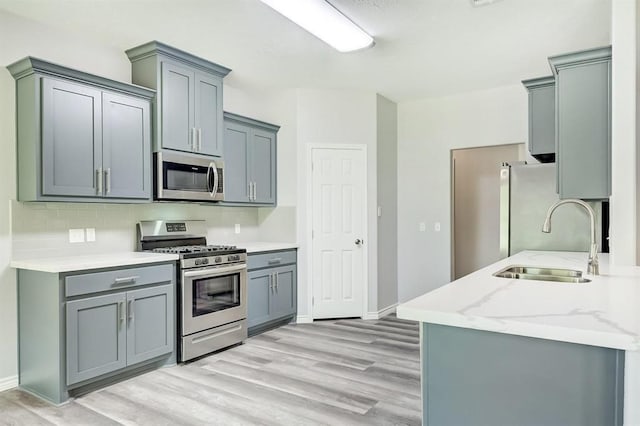 kitchen featuring sink, light hardwood / wood-style flooring, gray cabinetry, backsplash, and stainless steel appliances