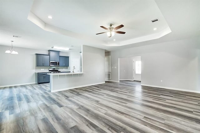 unfurnished living room featuring a tray ceiling, wood-type flooring, and ceiling fan with notable chandelier