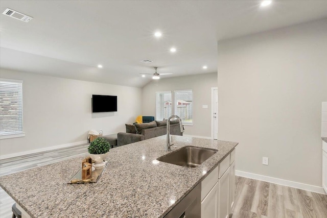 kitchen with sink, light stone counters, vaulted ceiling, an island with sink, and white cabinets