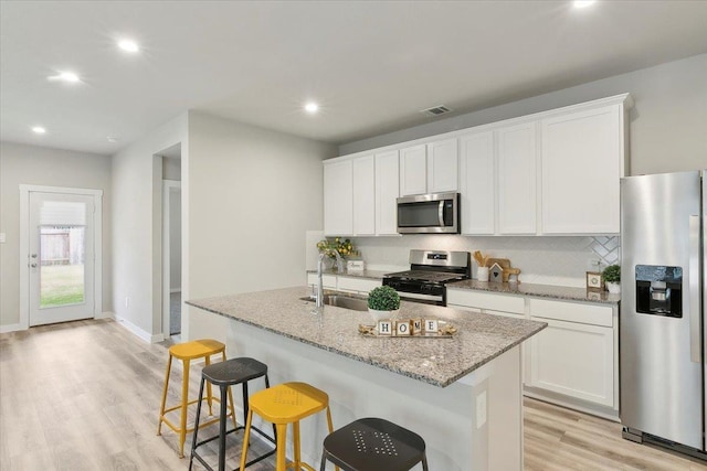 kitchen with sink, white cabinetry, stainless steel appliances, light stone countertops, and an island with sink