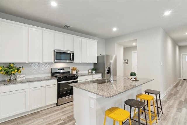 kitchen with white cabinetry, sink, a breakfast bar area, stainless steel appliances, and a center island with sink