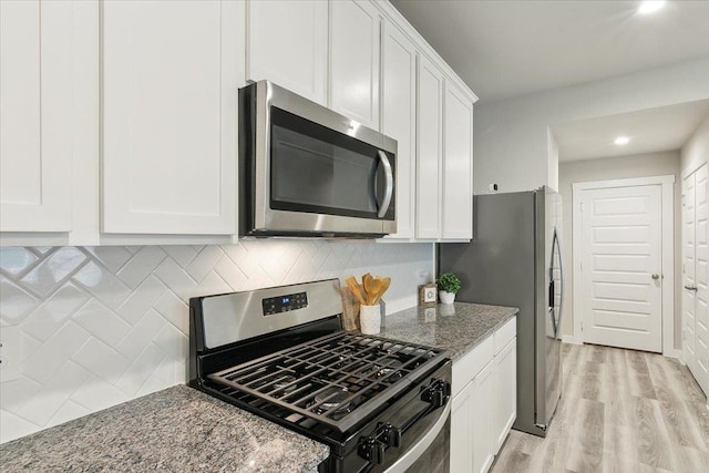 kitchen featuring appliances with stainless steel finishes, white cabinetry, backsplash, light stone countertops, and light hardwood / wood-style flooring