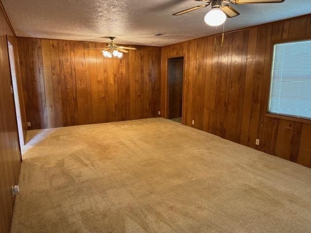 unfurnished room featuring carpet flooring, ceiling fan, a textured ceiling, and wooden walls