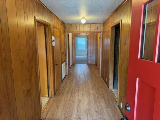 corridor with light wood-type flooring, a textured ceiling, and ornamental molding