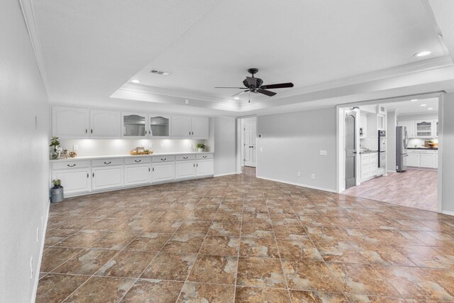 unfurnished living room with a tray ceiling, ceiling fan, and ornamental molding