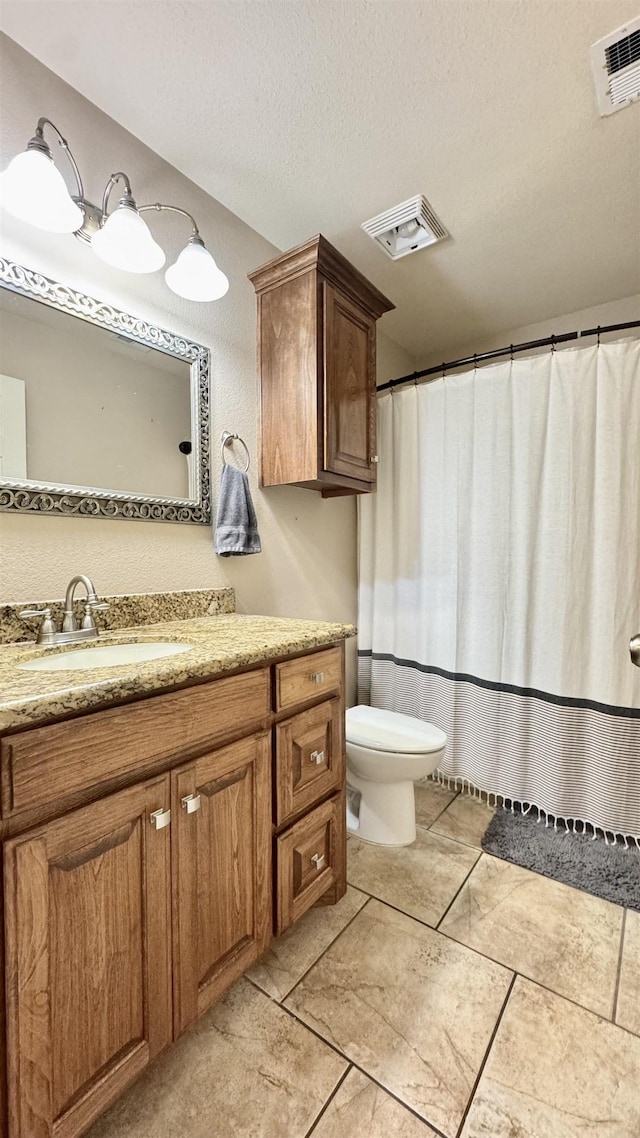 bathroom with a textured ceiling, toilet, vanity, and visible vents