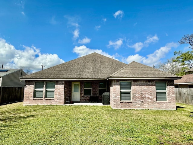 back of property featuring a shingled roof, fence, a lawn, and brick siding