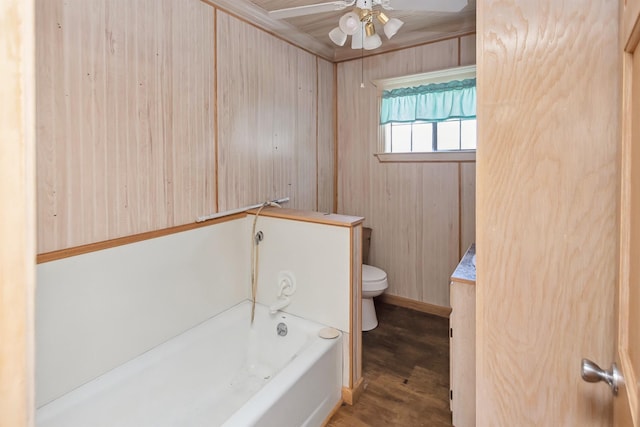 bathroom with a ceiling fan, toilet, wood finished floors, wood walls, and a bath