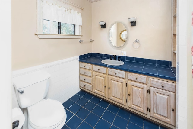 bathroom with tile walls, toilet, wainscoting, vanity, and tile patterned flooring