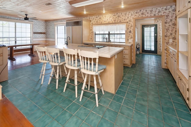 kitchen with an island with sink, wallpapered walls, a kitchen bar, and light countertops