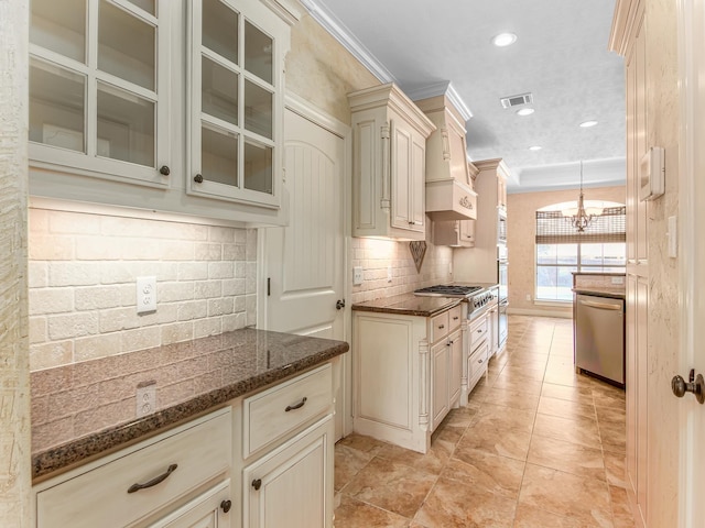 kitchen featuring dark stone counters, crown molding, appliances with stainless steel finishes, cream cabinetry, and decorative light fixtures