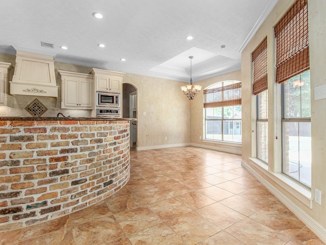 kitchen featuring custom range hood, stainless steel appliances, a raised ceiling, a notable chandelier, and cream cabinetry