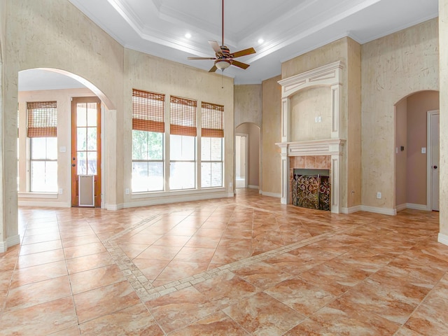 unfurnished living room with a tray ceiling, ceiling fan, crown molding, and a tiled fireplace