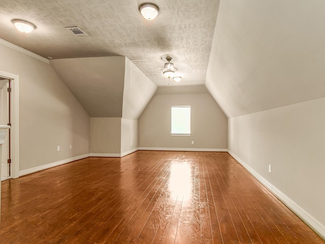 additional living space featuring vaulted ceiling, wood-type flooring, and a textured ceiling