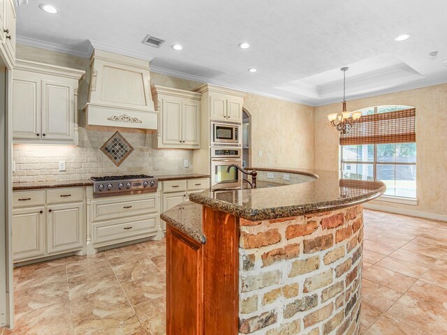 kitchen with hanging light fixtures, stainless steel appliances, a raised ceiling, a notable chandelier, and cream cabinetry