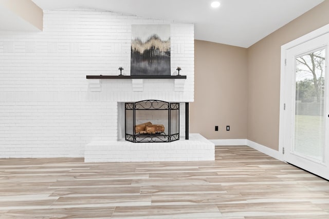 unfurnished living room featuring a brick fireplace, vaulted ceiling, and light hardwood / wood-style floors