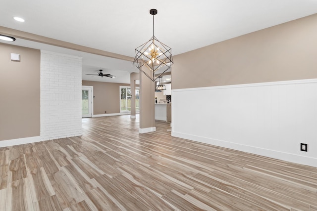 unfurnished living room featuring ceiling fan with notable chandelier and light hardwood / wood-style floors