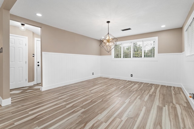 empty room featuring a notable chandelier and light hardwood / wood-style floors